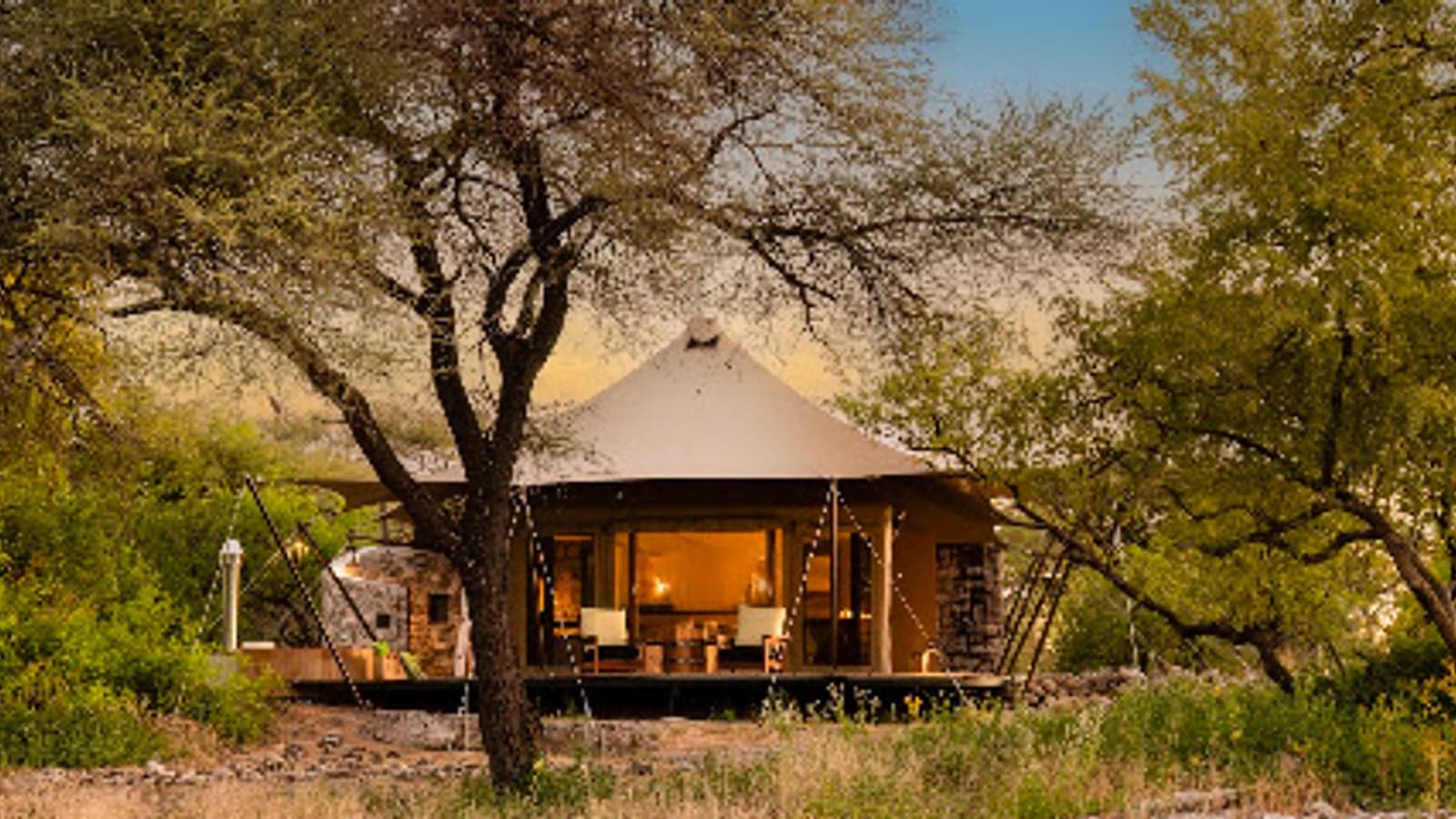 Eine Zeltsuite in der Abenddämmerung unter einem großen Baum, Onguma Tented Camp, Etosha