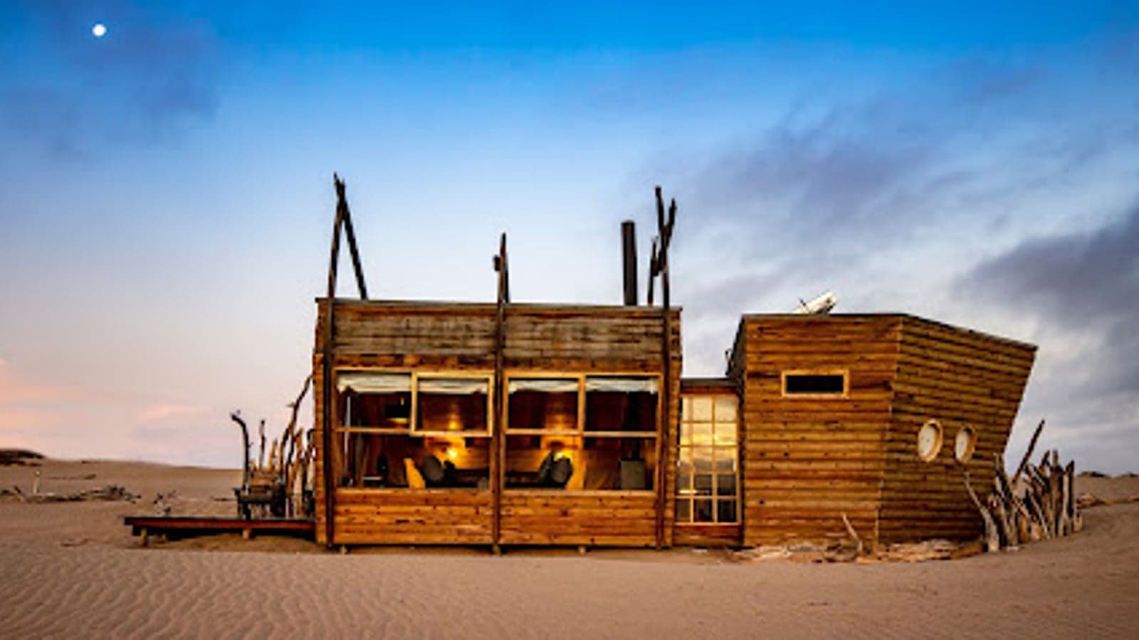 De scheepswrak-vormige chalets van Shipwreck Lodge op de duinen bij schemering